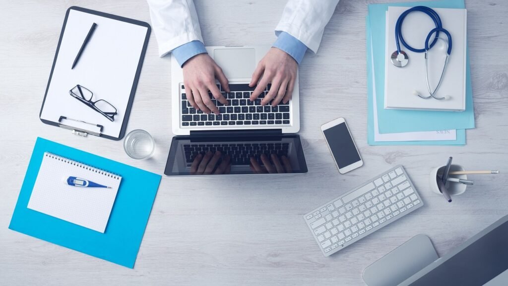 Clinician typing at a desk with a clipboard and stethoscope